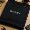 Minimalistisches schwarzes T-Shirt mit dem Spruch „DaSOURCE“ als kleiner Brustprint in weißer Serifenschrift